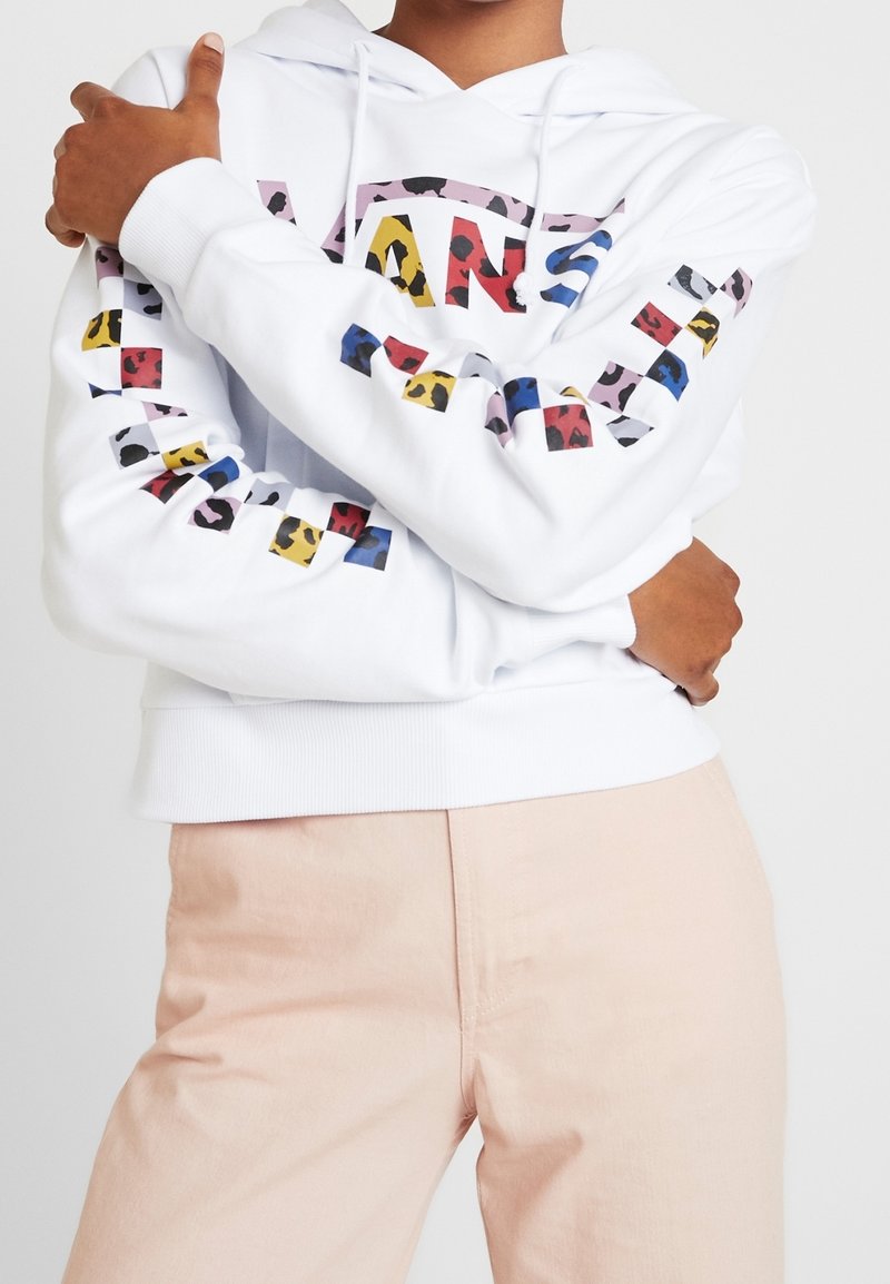 Sudadera blanca con texto gráfico multicolor y patrones en las mangas. Combinada con pantalones rosa claro. Tela suave, ajuste regular y capucha ajustable.