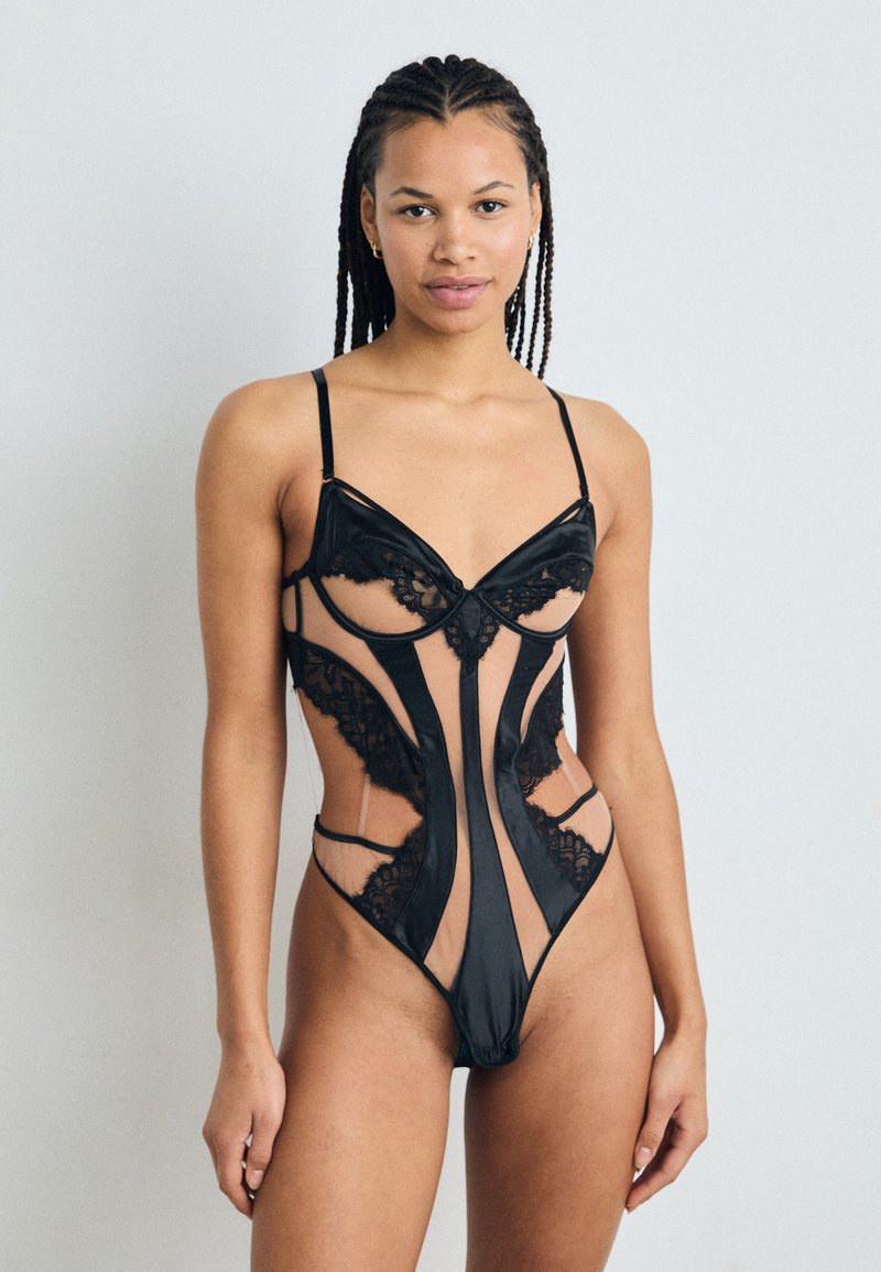Must mustriba musta pitsiline bodysuit, millel on vormitud tassid, lõigatud sektsioonid, õhukesed rihmad ja lillepitsist aktsendid, mis rõhutavad selle keerukat disaini.