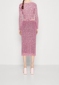 Růžový top s dlouhým rukávem a květinovým vzorem spojený s ladící midi sukní, obě vyrobené z průsvitné látky. Dolní okraj je vlnkovaný. Na nohou jsou podpatkové muly.