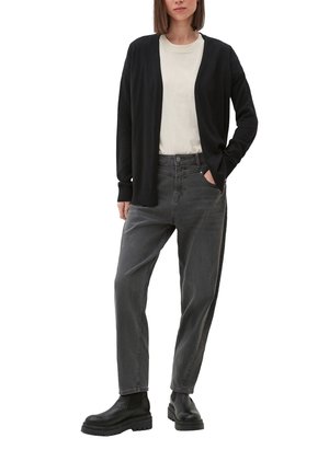 Cardigan noir sur un t-shirt crème, associé à un jean taille haute gris et des bottes noires épaisses. Présente une coupe décontractée et un design minimaliste.