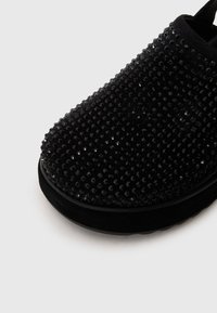 Schwarzer Slipper mit strukturierten Oberflächen, verziert mit runden Pailletten, abgerundetem Zeh und gepolstertem Schuhsohle.