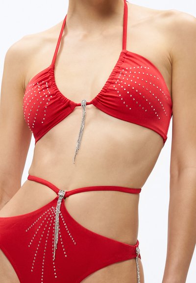 Červený bikini set s trojuholníkovým vrchným dielom zdobeným kamienkami a stredovým dekoratívnym prvkom, ktorý zvýrazňuje priliehavú a hladkú textúru.