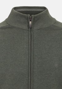 Mörkgrön zip-up tröja med hög ribbad krage och textilier med struktur. Har en kontrasterande randig innersida och en liten logotyp på bröstet.