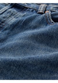 Tissu en denim bleu profond avec une texture douce, présentant des coutures visibles de couleur orange contrastante et un léger délavage à certains endroits.