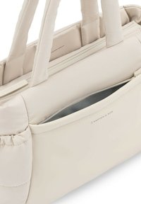 Sac fourre-tout en crème clair, fabriqué dans un matériau doux et texturé. Dispose de deux poignées, d'une poche zippée et d'un logo discret sur le côté.