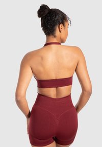 Maroon sport-bra en set met hoge taille shorts, gemaakt van rekbaar materiaal, met een halterband en een open rugontwerp. Gladde textuur.