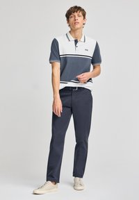 Piké i mörkblått och vitt med horisontella ränder, korta ärmar och klassisk krage, i kombination med mörka byxor och sneakers.