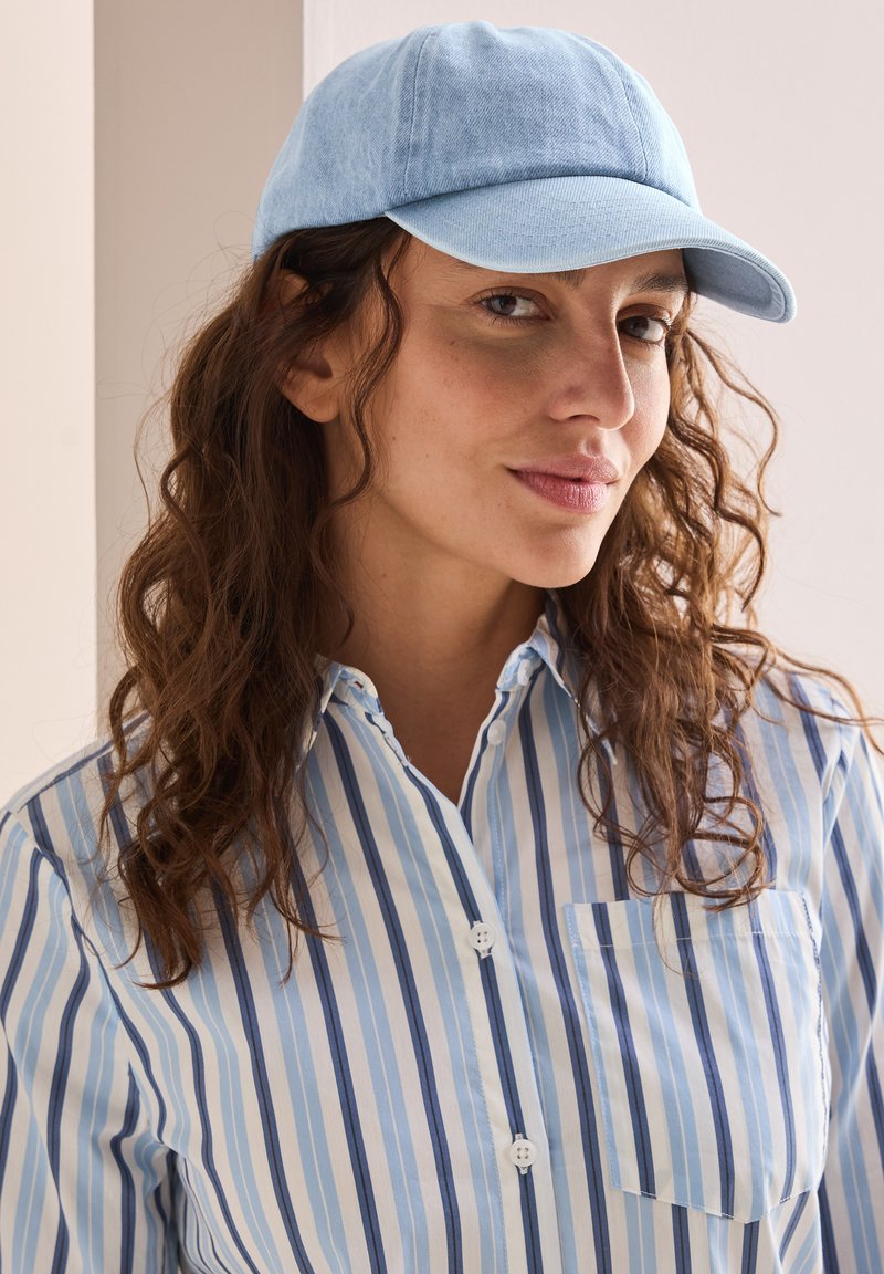Gorra de béisbol de algodón azul claro con corona redondeada y visera corta, combinada con una camisa de botones de rayas azules y blancas.