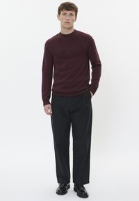 Maglione a maglia color vino con un design a yoke testurizzato, abbinato a pantaloni neri. Il maglione presenta un colletto rotondo e polsini a coste.