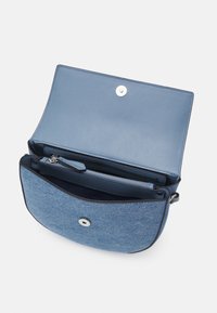 Blå denim- och lädercrossbody-väska med magnetstängning, inre dragkedjeficka och slät textur. Har en rundad form och kontrasterande detaljer.
