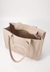 Borsa tote in tela beige con doppie tracolle, tasca interna con zip e branding stampato sul davanti. Texture liscia e design spazioso.