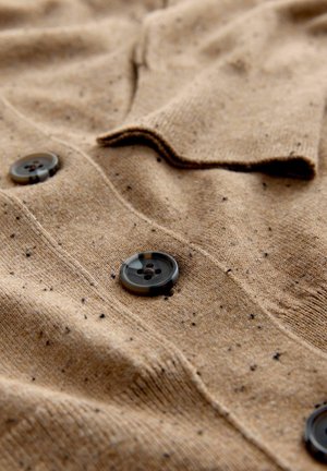 Beige Strickcardigan aus strukturiertem Stoff mit gepunkteten Details und schwarzen Knöpfen. Er verfügt über einen engen Kragen und eine Knopfleiste vorne.