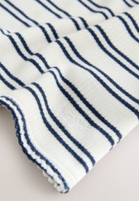 Bela tkanina z mornarsko modrimi črtami, z rebrasto teksturo in valovitim robom. Vključuje subtilno izvezeno oznako "NEXT".