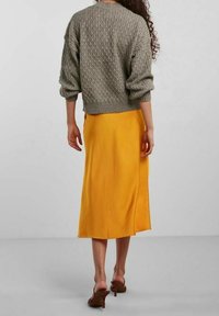 Harmaa neulottu villapaita, jossa on teksturoitu kuvio, yhdistettynä laskeutuvaan keltaiseen midihameeseen, jossa on sivuhalkio. Ruskeat korkokengät.