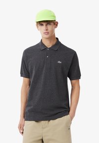 Kolgrå pikétröja med krage och korta ärmar, försedda med en liten vit Lacoste-logotyp. Matchas med en ljusgrön keps.