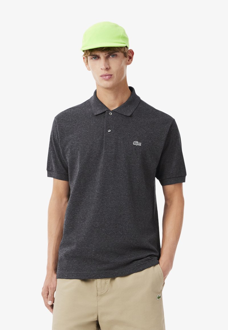 Kolgrå pikétröja med krage och korta ärmar, försedda med en liten vit Lacoste-logotyp. Matchas med en ljusgrön keps.