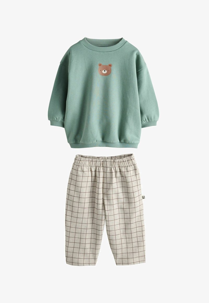 Hanorac verde din fleece cu un grafic de urs pe piept, asortat cu pantaloni din bumbac bej cu carouri, având un talie elastică.