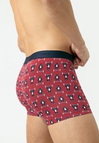 Boxer-briefs rouges avec un motif répétitif de dessins animés d'ours soulevant des poids, présentant une ceinture marine et un ajustement serré. Matériel en coton doux.