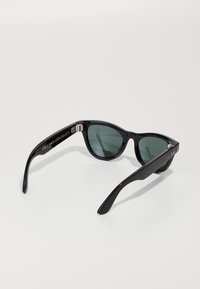 Occhiali da sole Ray-Ban con montatura nera e lenti verde scuro, braccia ripiegate e logo del marchio visibile sulla tempia destra, su uno sfondo bianco.