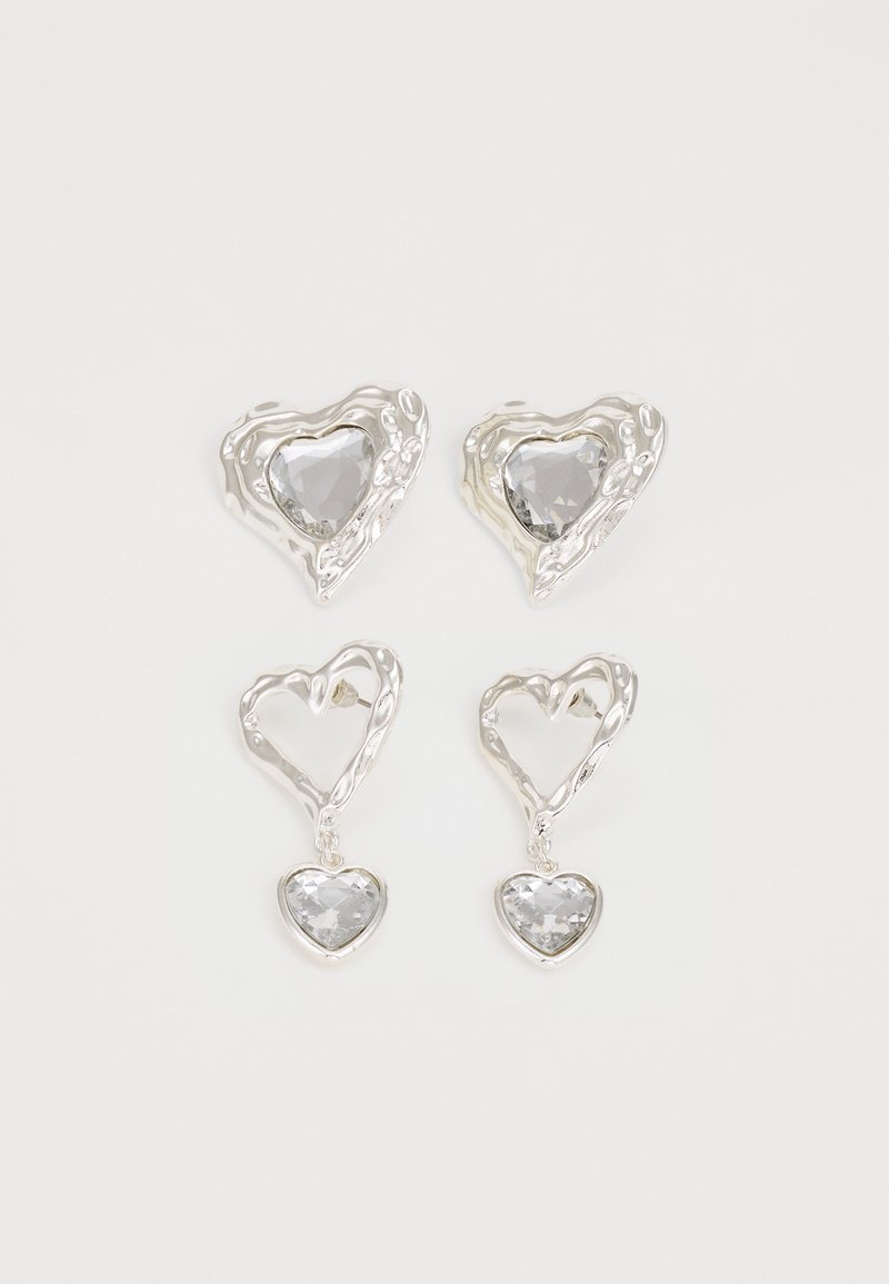 Des boucles d'oreilles en argent en forme de cœur présentent des pierres claires facettées, avec un cadre texturé. L'ensemble comprend des styles à clou et des styles pendants.