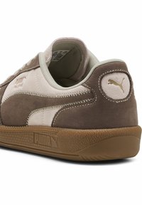 Zapatillas de ante marrón con acentos en rosa claro, cordones beige y una suela de goma texturizada. Presenta un diseño cosido y un logo embosado en el talón.