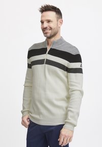 Men's pullover sweater in light cream with black and gray horizontal stripes, zippered collar, ribbed cuffs, and textured knit fabric.