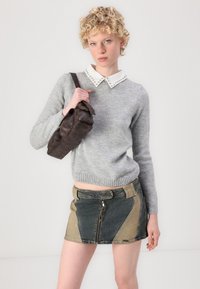 Pulover tricotat gri cu un guler alb cu ținte, asociat cu o fustă mini din denim multicolor. Modelul ține o geantă de umăr din piele maro.