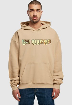 Beige hoodie featuring a graphic "LOS ANGELES" across the chest, with a front pocket and ribbed cuffs. Soft fabric and relaxed fit.