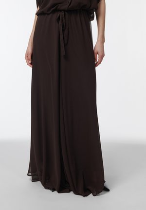 Pantalones negros de pierna ancha con cintura atada, tela fluida que llega hasta el suelo, combinados con zapatos negros puntiagudos.