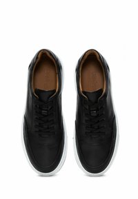Zapatillas negras de cuero con una textura suave, con un diseño simple, suelas de goma blanca y cordones negros. El interior tiene un forro en tonos marrones.