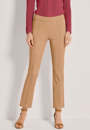 Beige, rekbare broek met een smalle pasvorm, voorzien van verticale naaddetails en een elastische tailleband, gecombineerd met bruine hoge hakken.