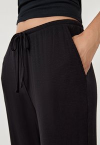 Czarne, prążkowane spodnie dresowe z elastycznym pasem, regulacją sznurka i boczną kieszenią, prezentujące gładką fakturę materiału.