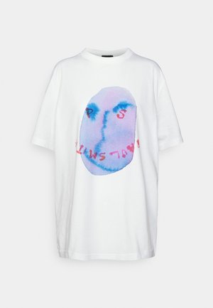 T-shirt en coton blanc à coupe ample, présentant une grande illustration abstraite de visage en nuances de bleu et de rose, avec un texte rouge en dessous.