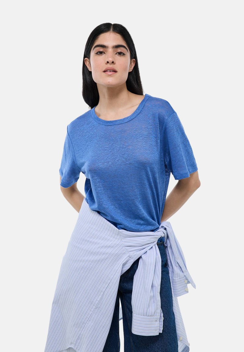 T-shirt bleu à manches courtes en tissu léger et légèrement transparent. Associé à une chemise à rayures claires nouée autour de la taille.