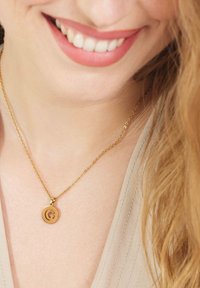 Gouden ketting met een ronde hanger met een letter "G." Delicate ketting met een soepele textuur, prominent gedragen op blote huid.