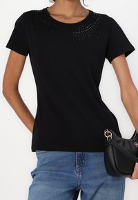 Camiseta negra de manga corta con un escote texturizado y adornado, y un diseño ajustado. Acompañada de un bolso negro.