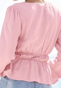 Rosa blus med rund halsringning och puffärmar. Har elastisk midja och flödande nederkant. Mjukt, lätt tyg med en slät textur.