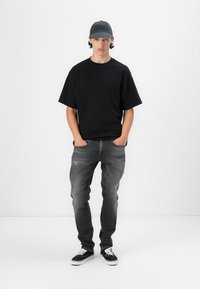 Tricou negru cu mânecă scurtă, blugi gri cu croială slim, adidași negri și o căciulă de culoare albastru închis. Design minimalistic fără modele sau embellishments vizibile.