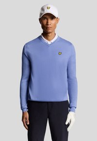 Maglione lavorato a maglia di colore azzurro chiaro con scollatura a V, caratterizzato da un piccolo logo giallo. Indossato con una camicia a colletto bianco e un cappellino bianco, completato da un guanto bianco.