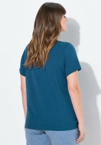 Lyhythihainen, teal-värinen t-paita, jossa on rento leikkaus, pyöreä pääntie ja pehmeä rakenne; yhdistetty vaaleansinisiin housuihin.
