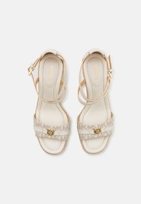 Beige leather sandals with a multi-patterned MK logo strap and gold hardware detail. Features ankle straps and cushioned footbeds.