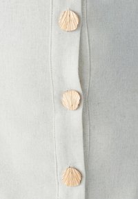 Beige linnen stof met drie decoratieve knopen in de vorm van schelpen met gedetailleerde texturen die verticaal langs de rand lopen.