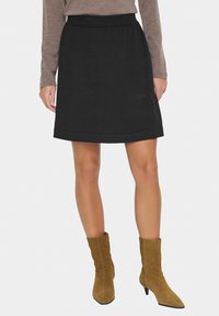 Jupe noire en ligne A avec une texture lisse et un ourlet replié. Associée à des bottines en daim beige à bout et talon pointus.