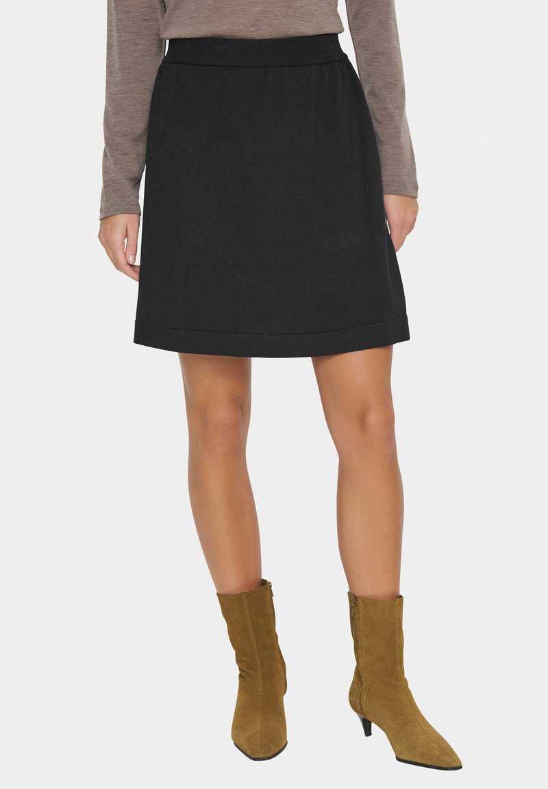 Jupe noire en ligne A avec une texture lisse et un ourlet replié. Associée à des bottines en daim beige à bout et talon pointus.