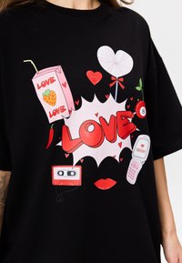 Czarny T-shirt z wyrazistymi grafikami, w tym sercami, kartonem napoju, kasetą i telefonem komórkowym, skupiający się na słowie "MIŁOŚĆ."