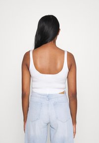 Camiseta corta de canalé blanca con tirantes anchos, espalda baja y diseño sin costuras, combinada con jeans de tiro alto en un lavado claro que cuentan con bolsillos en la parte posterior.