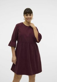 Burgundska obleka iz mehkega, teksturiranega blaga, ima tričetrtinske zvonaste rokave, naguban pas in raztegnjeno krilo.