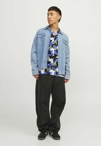 Jeansjakke med to brystlommer, båret over en flerfarvet blomsterbluse i blå, sort og hvid, parret med løse sorte bukser og sneakers.