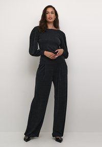 Schwarzes zweiteiliges Outfit mit einem strukturierten, langärmligen Oberteil mit einem Bootsausschnitt und weit geschnittenen Hosen. Der Stoff hat subtile Muster und einen sanften Glanz.