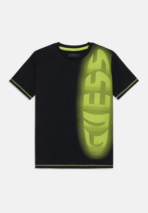 Black cotton t-shirt featuring a large green "GUESS" logo gradient on the front, with green stitching on the collar and sleeves.